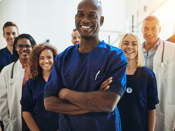 Young African male doctor smiling while standing in a hospital corridor with a diverse group of staff in the background