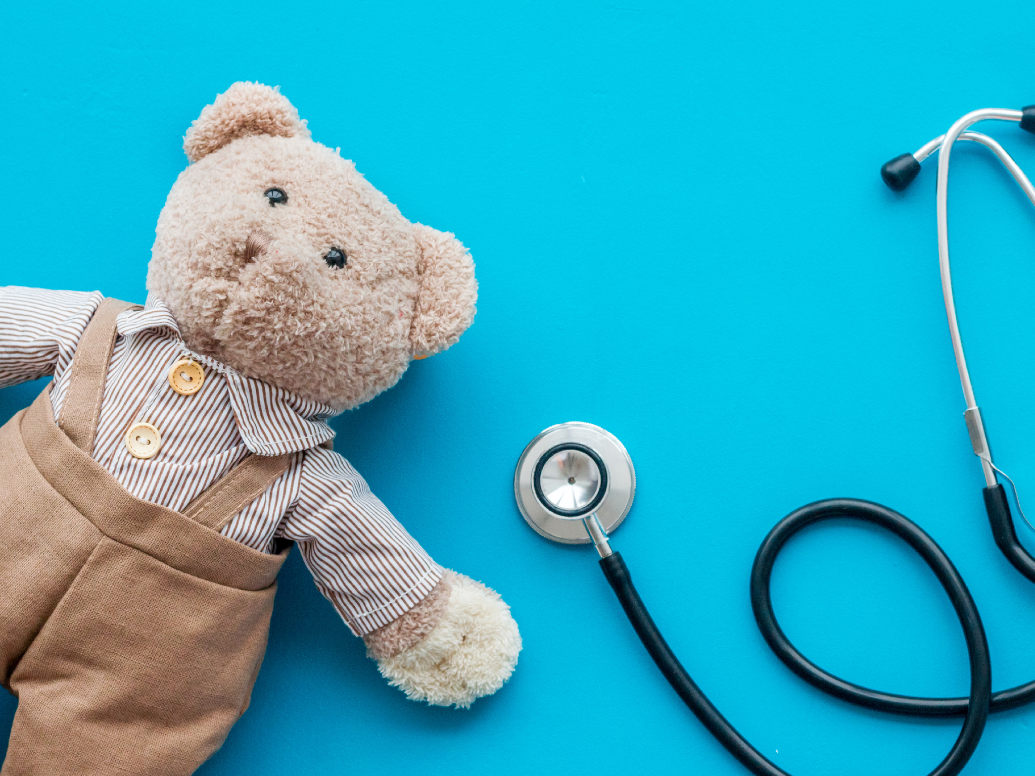 Children's doctor concept. Teddy bear toy and stethoscope on blue background top view.