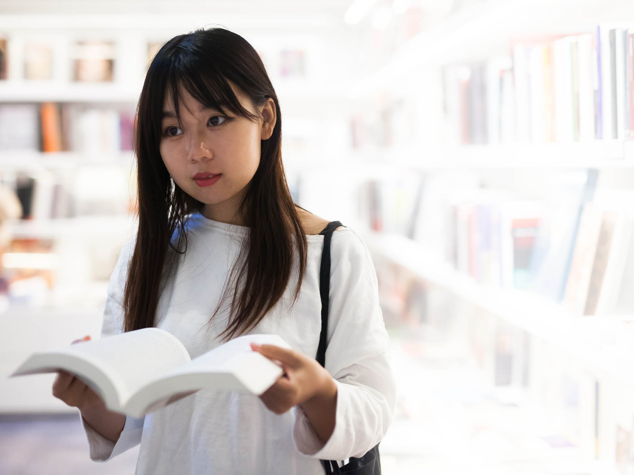 Young female student choosing new books on shelves in library
